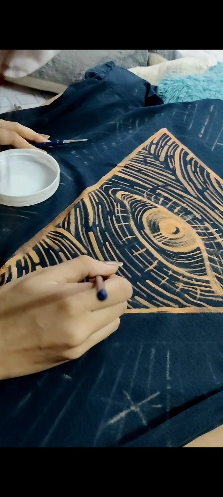 two hands are working on a t - shirt that has an eye drawn on it