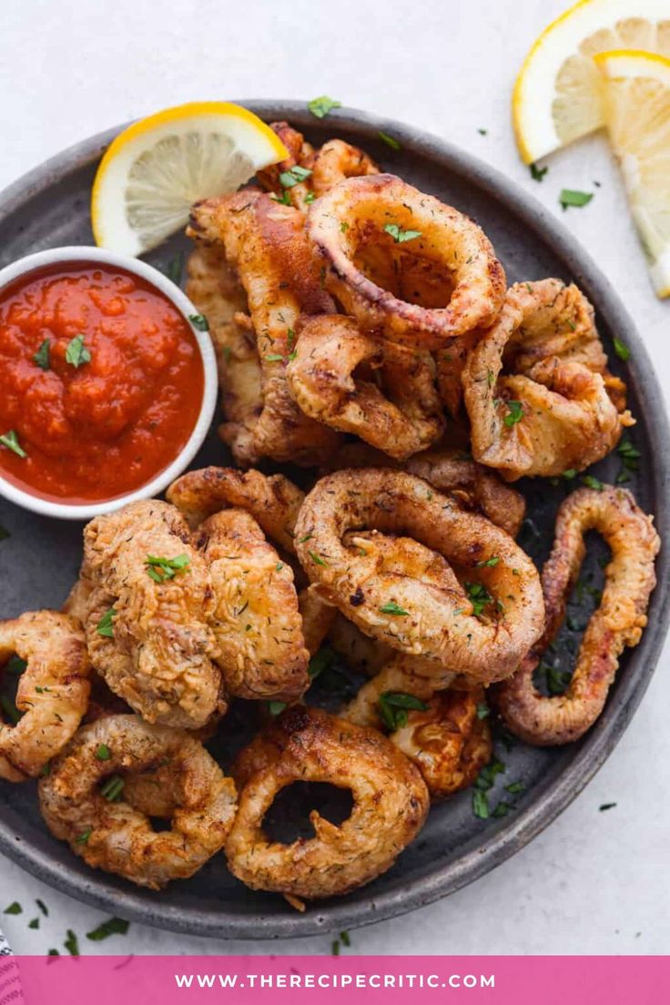 fried octopus rings on a plate with ketchup and lemon wedges