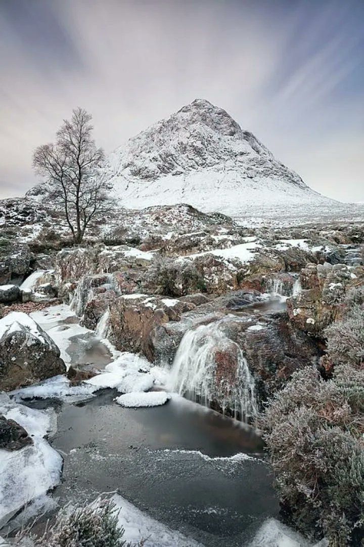 a snowy landscape with water and trees in the foreground