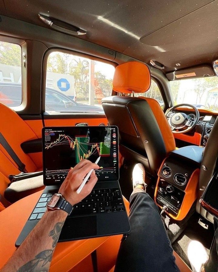 a man sitting in the back seat of a car using a laptop computer and holding a pen