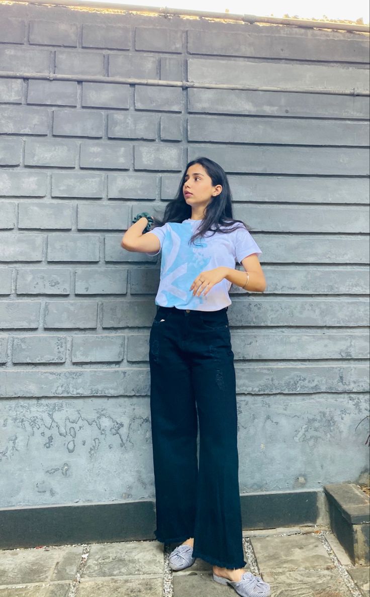 a woman leaning against a wall with her hands on her hips and looking up at the sky