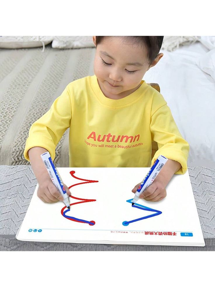 a little boy that is sitting at a table with some scissors in his hand and writing on the paper