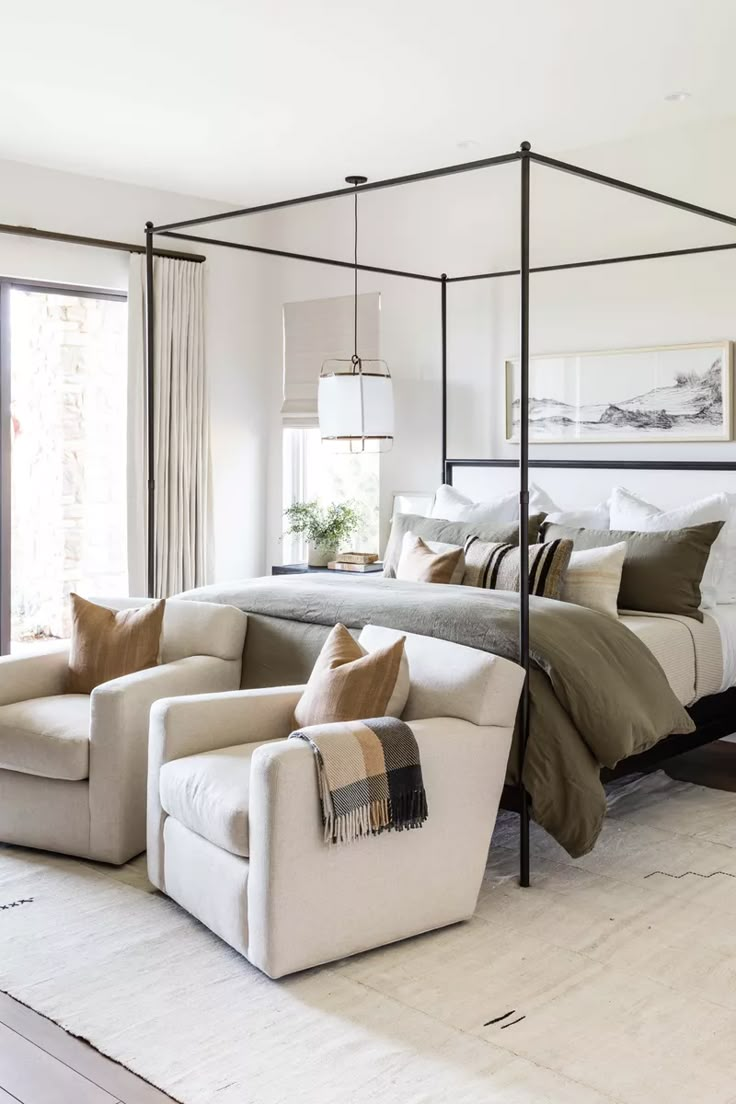 a bedroom with four poster bed, white couch and beige chair in front of it