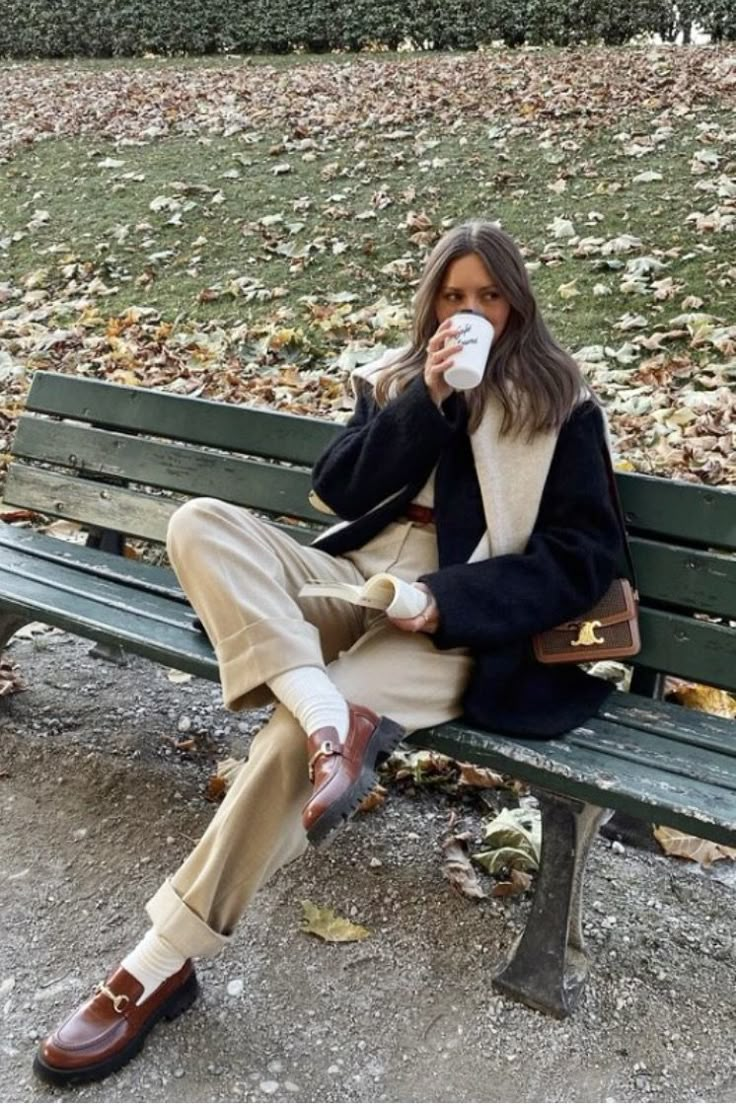 a woman sitting on a bench drinking from a cup