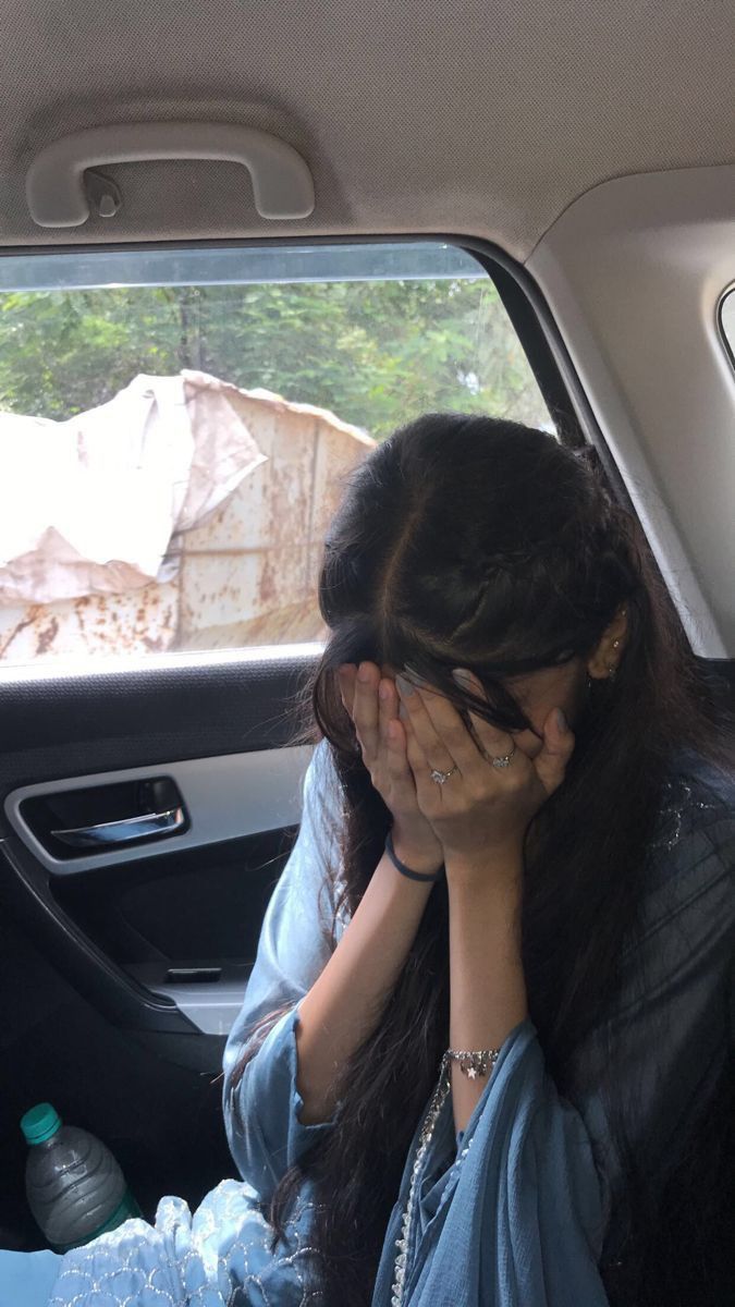 a woman sitting in the back seat of a car holding her hands to her face