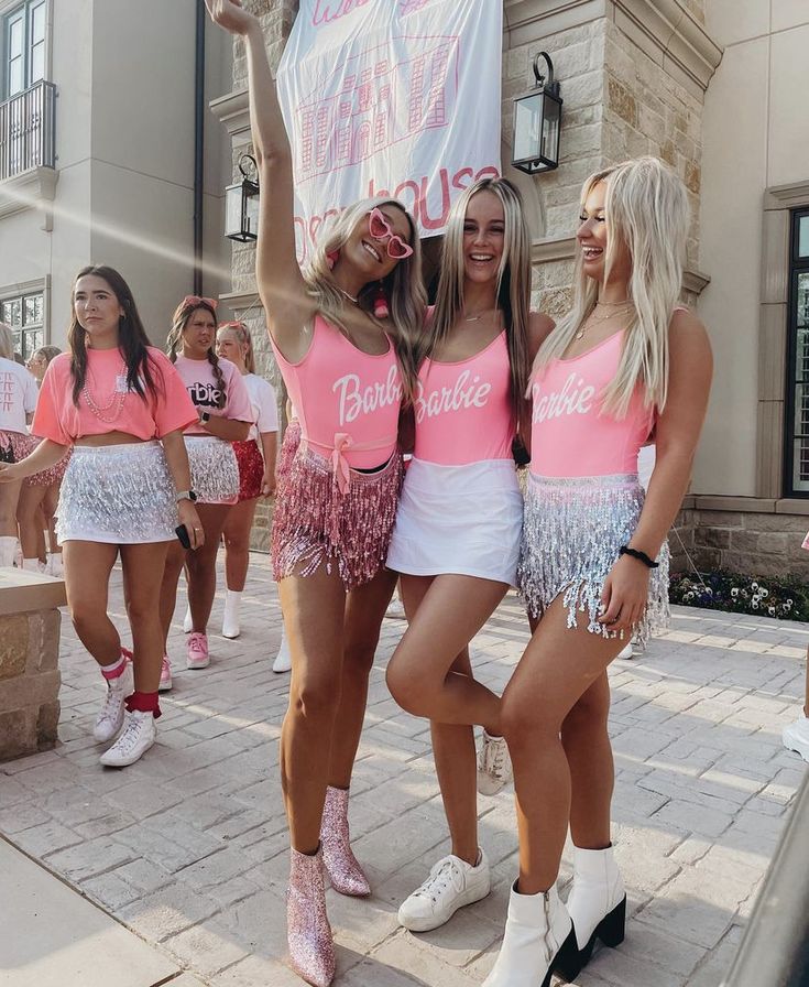 three women in pink and white cheerleader outfits posing for the camera while holding up a sign