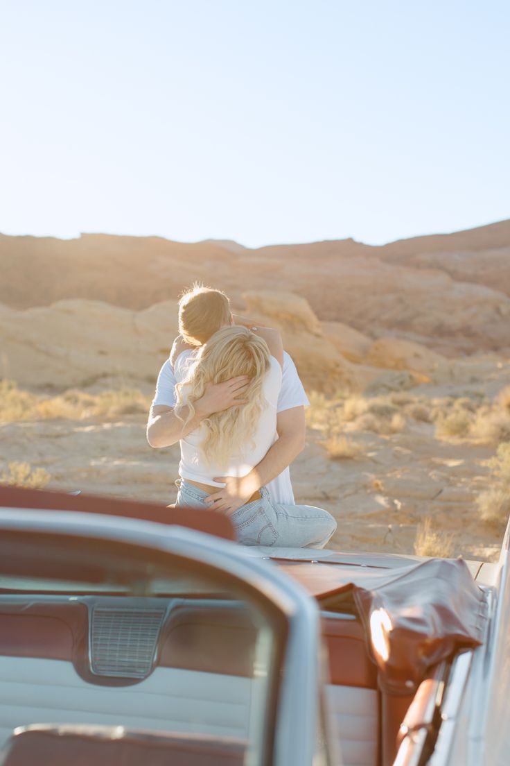 a man and woman sitting on the back of a pick up truck in the desert