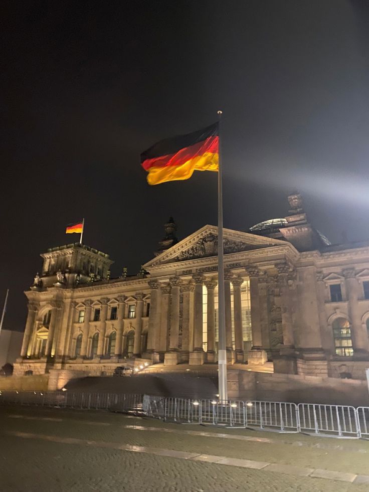 the german flag is flying in front of an old building at night with lights on