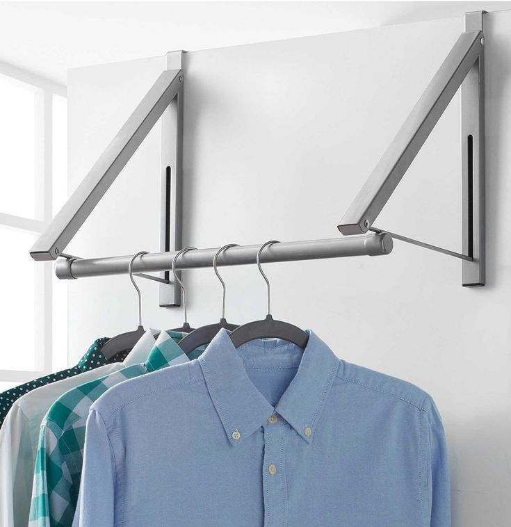 three shirts are hanging on a rail in front of a window, and one is blue