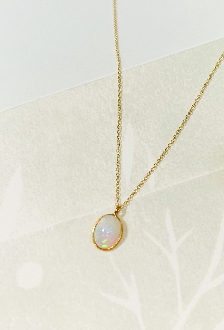 "Oval Opal necklace Oval Opal bezel set pendant on a double rope dainty chain. Charm pendant is made in 18k gold set on a dainty 14k Yellow Gold double rope chain. Necklace length is 16\" and sits under your clavicle. A perfect necklace that is beautiful all year round. + Ethiopian Opal Charm * 9x11mm  + 18k Gold bezel finish + 14k Yellow Gold Double Rope chain. + Approx. 16\" chain + Comes packaged in our signature box + Please note all Mantle 14k gold pieces are made-to-order. In stock items s Gold Dainty Necklace Black Opal, Gold Opal Necklace, White Pendant Necklace With Bezel Setting, White Bezel Setting Necklace For Gift, Birthstone Necklace With Round Pendant On Cable Chain, Gold Necklaces With Bezel Setting For Gift, Oval Pendant Yellow Gold Necklace For Her, White Pendant Jewelry With Bezel Setting, 14k Gold Oval Necklace For Gift