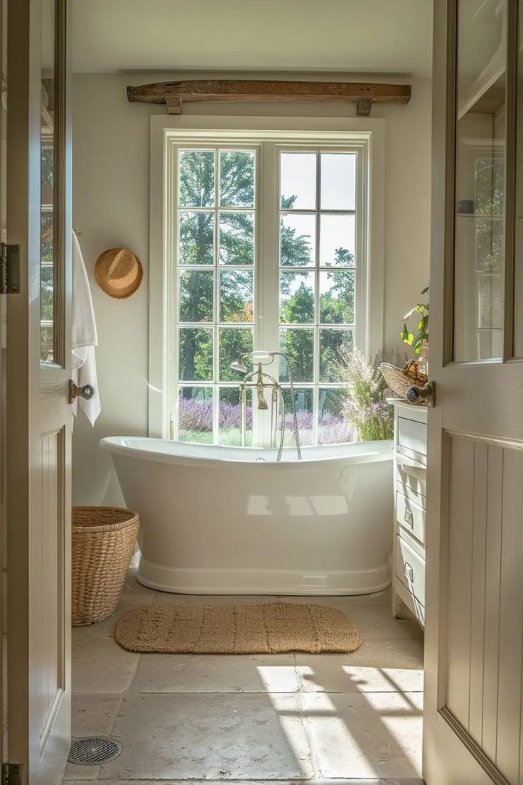 a white bath tub sitting under a window next to a sink in a bathroom with a rug on the floor