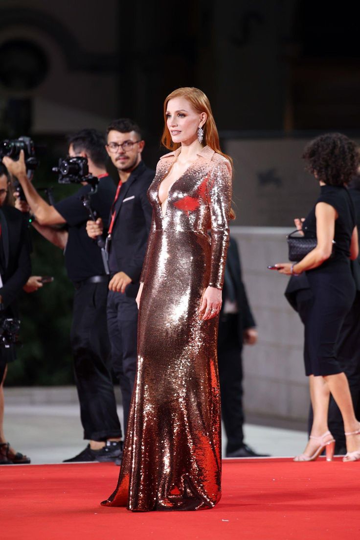 a woman standing on top of a red carpet next to other people and taking pictures