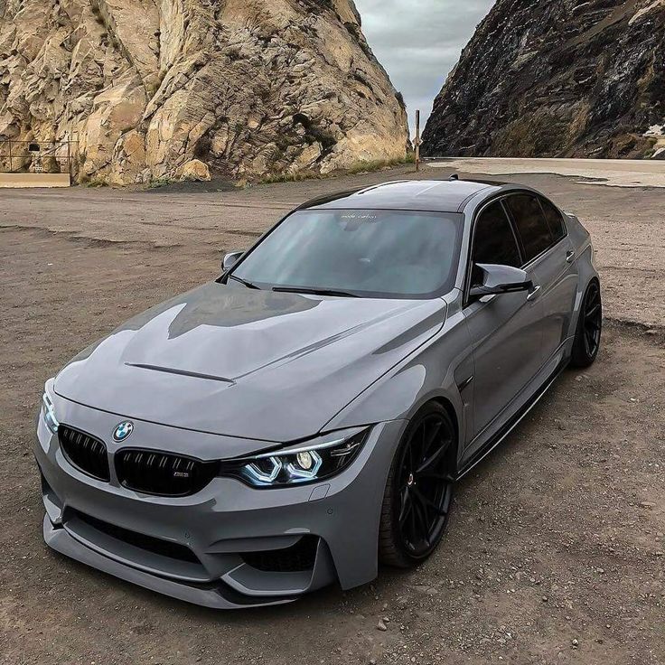 a grey bmw is parked in front of some rocks