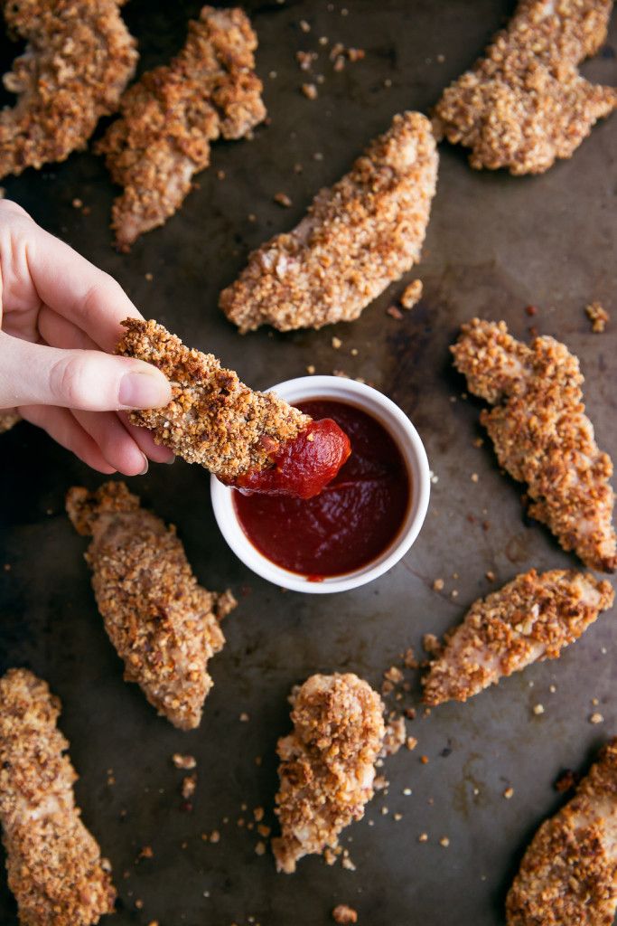 someone is dipping something into a small white bowl with ketchup on it and fried chicken wings in the background