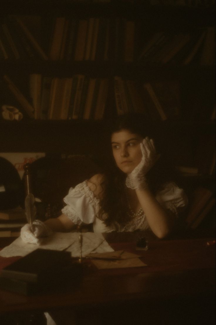 a woman sitting at a table in front of a bookshelf