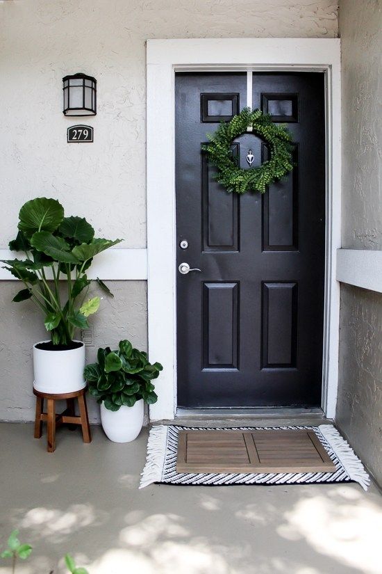 a black front door with a wreath and potted plants