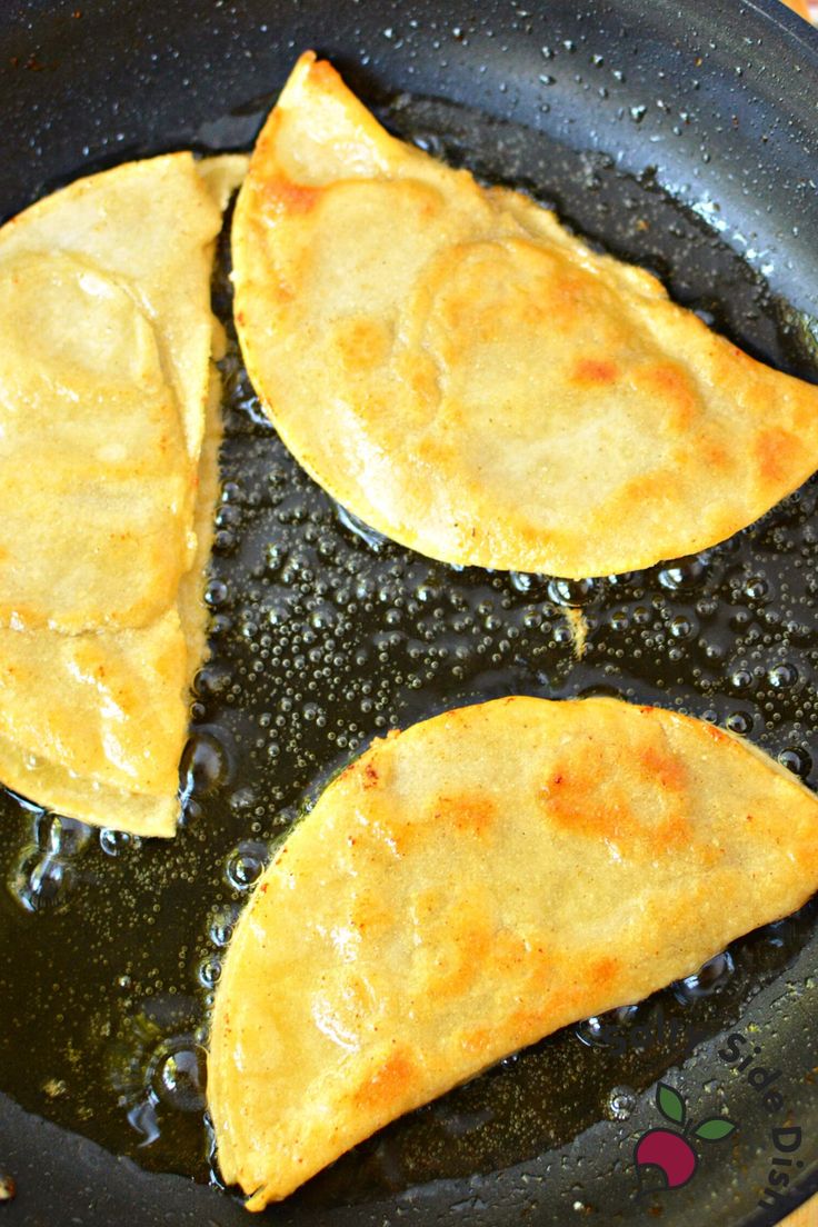 three quesadillas frying in a skillet with oil on the side