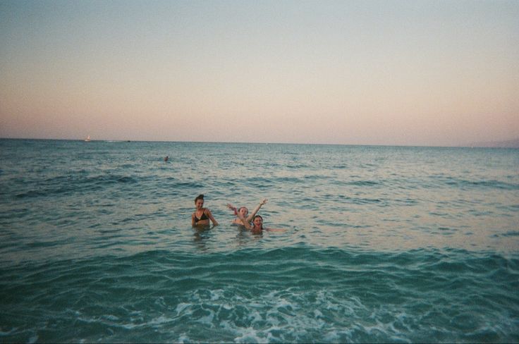 two people swimming in the ocean at sunset