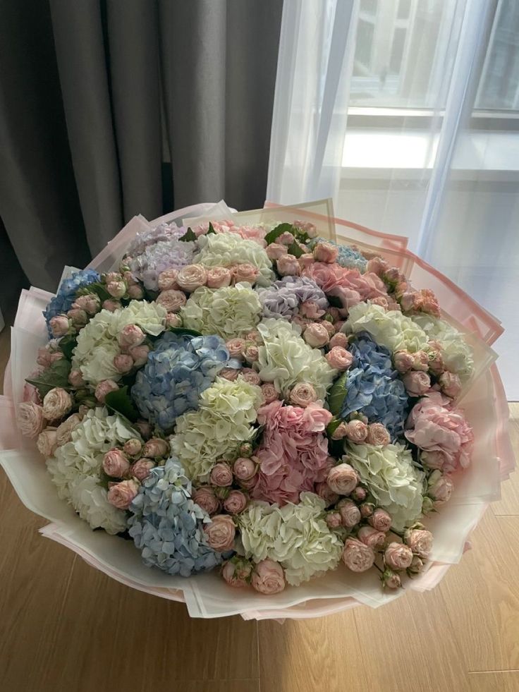 a bouquet of flowers sitting on top of a wooden table next to a window with curtains