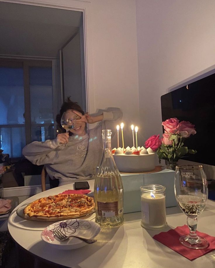 a woman sitting at a table in front of a pizza and wine glass with candles on it