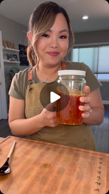 a woman holding a jar of honey on top of a wooden table