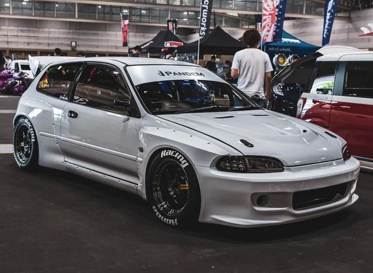 a white car is parked in front of other cars at an auto show with people looking on