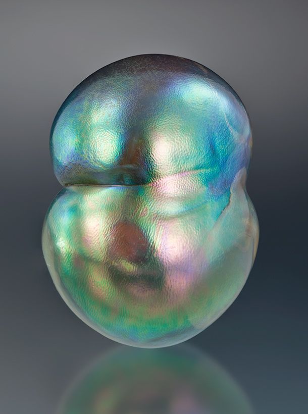 an iridescent pearl is shown in the middle of a gray background, with its head resting on it's side