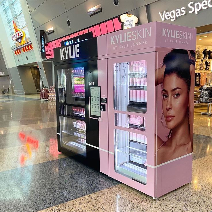 a pink kiosk in an airport terminal with advertisements on the wall behind it