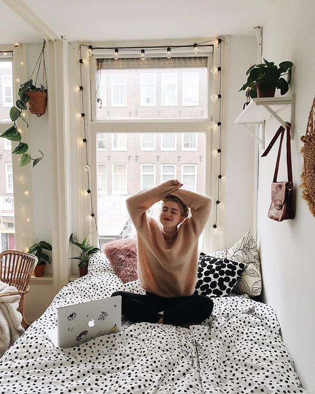 a woman sitting on top of a bed in front of a window next to a laptop computer