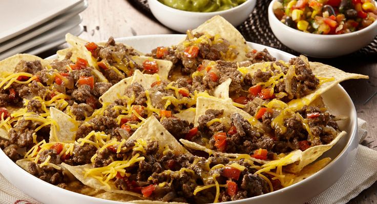 a white bowl filled with beef nachos next to bowls of salsa and tortillas