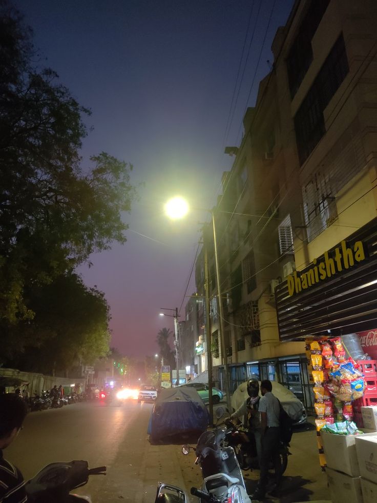 people are walking down the street in front of some stores at night time, with one person holding an umbrella