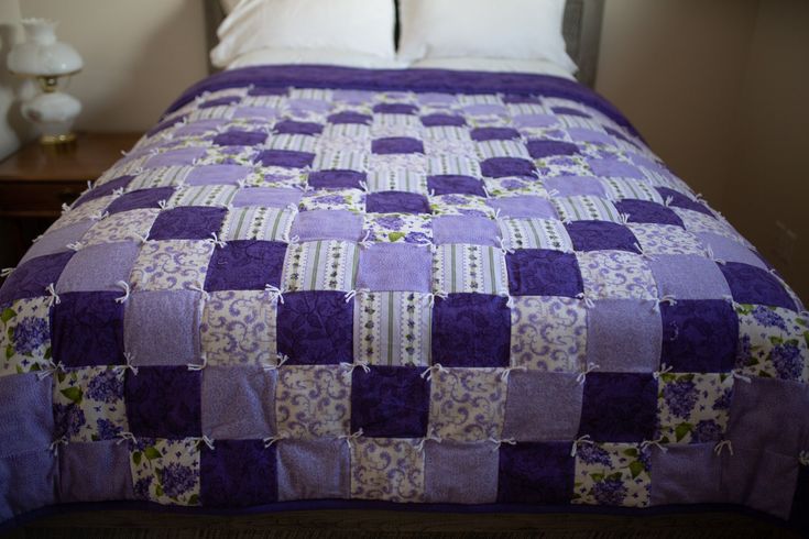 a purple and white quilted bed in a room with two lamps on either side