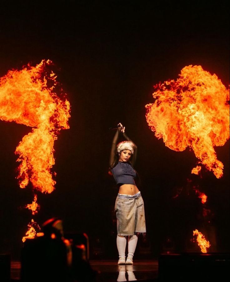 a woman standing on top of a stage in front of large fire balls behind her