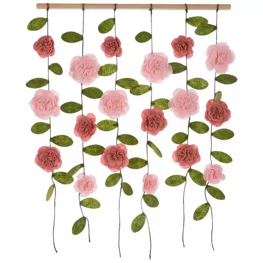 some pink flowers and green leaves hanging from a wooden frame on a white wall ornament