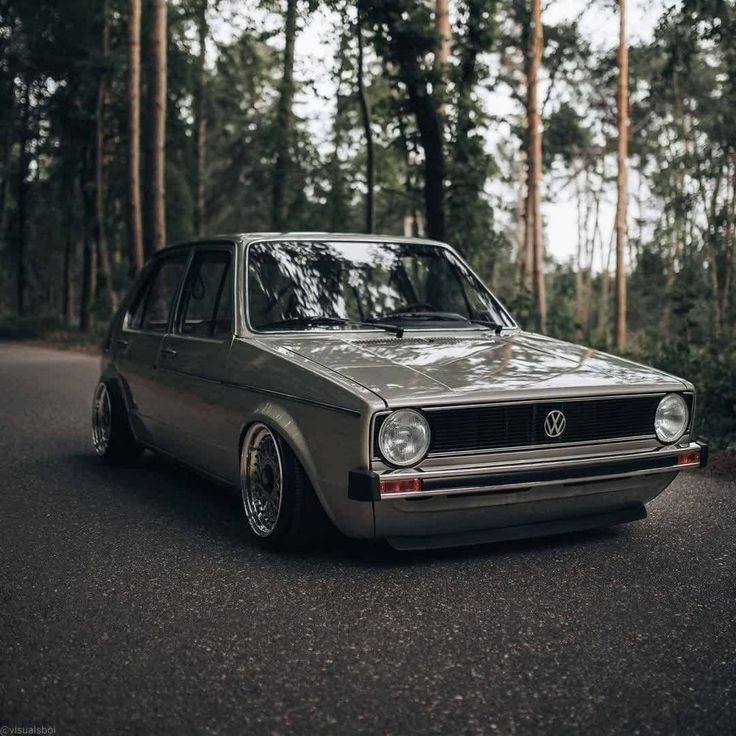 an old car is parked on the side of the road in front of some trees