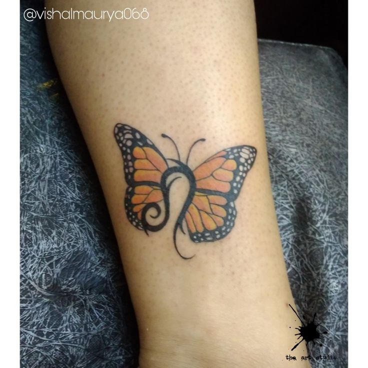 a small butterfly tattoo on the ankle is shown in black and orange colors with swirls