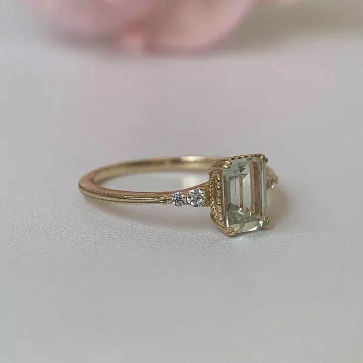 a close up of a ring on a table with a flower in the background and a pink rose behind it