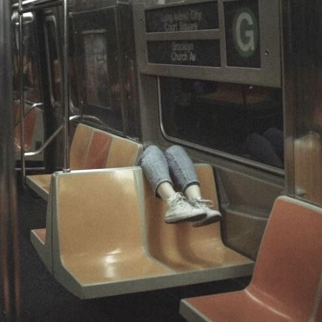 a person sitting on a subway train seat with their feet propped against the rail rails