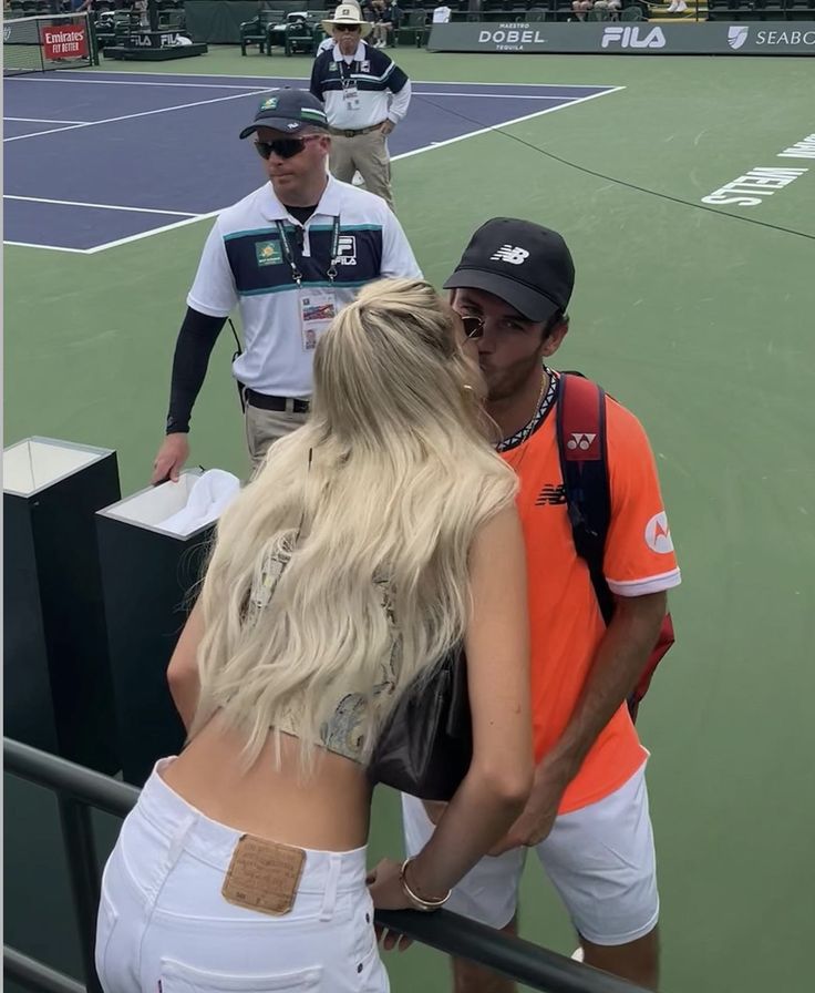 a woman in white shorts and an orange shirt is talking to a man on a tennis court