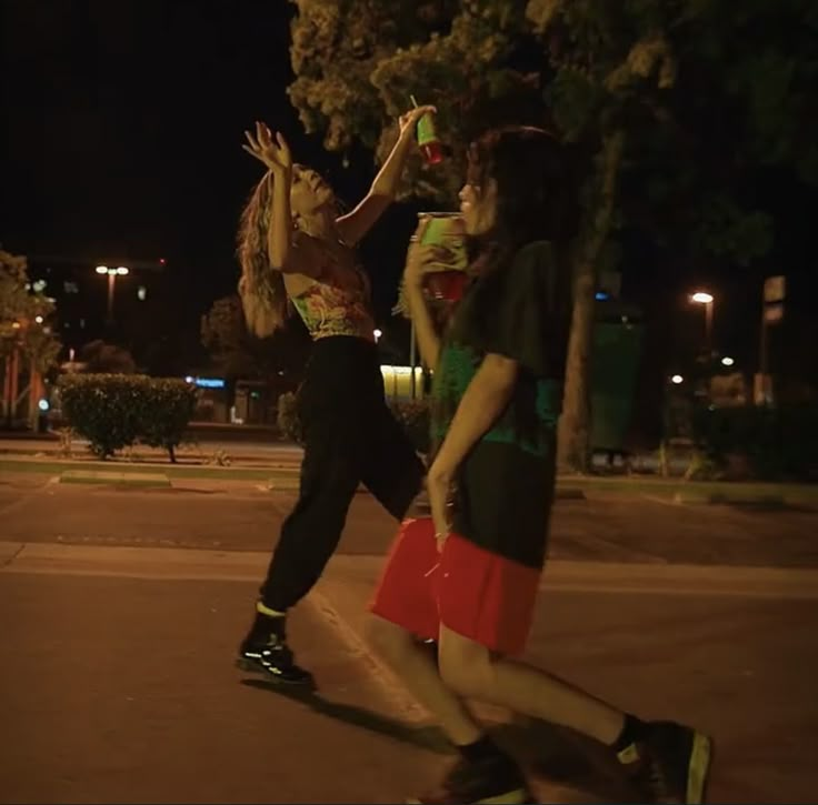 two people are playing basketball on the street at night, one is reaching for the ball