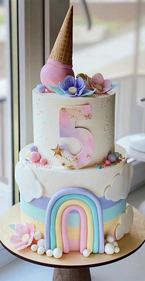 a multi layer cake with a unicorn horn on top and rainbow decorations around the base