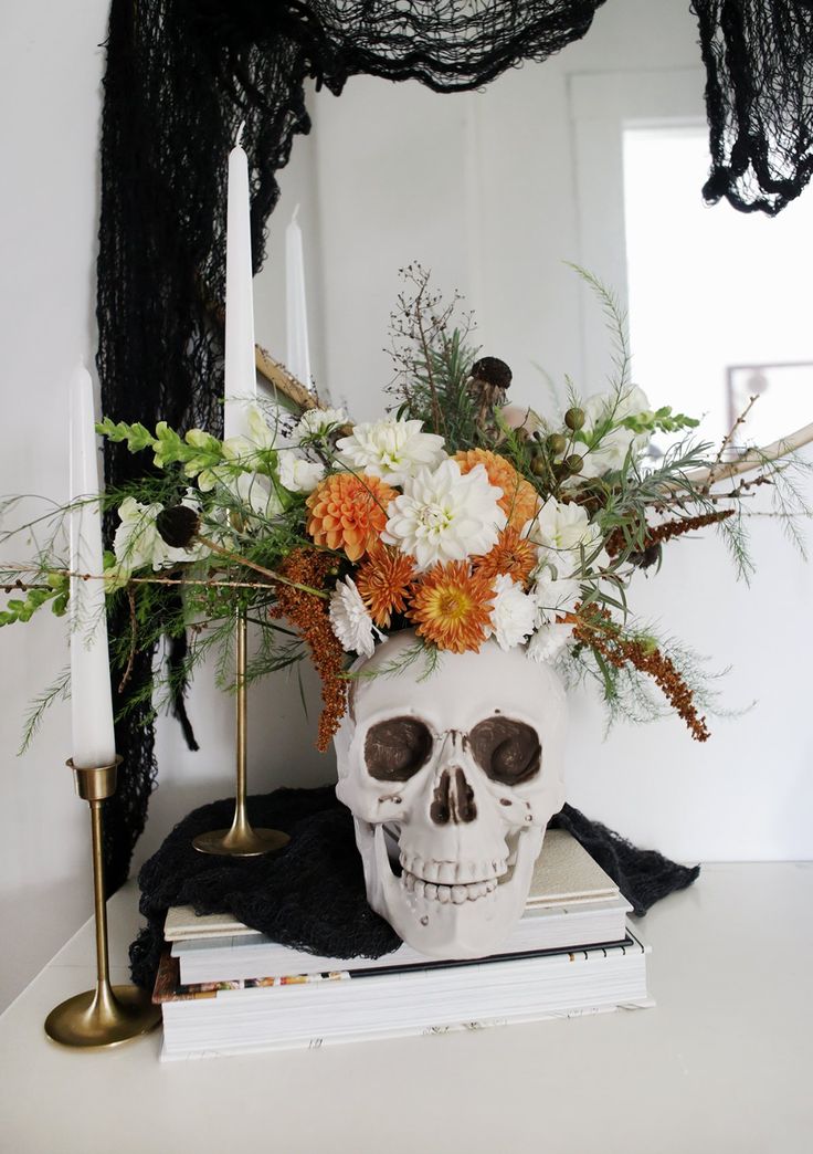 a white skull with flowers in it sitting on top of a stack of books next to a candle