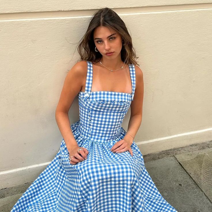 a woman in a blue and white checkered dress sitting on the ground next to a wall