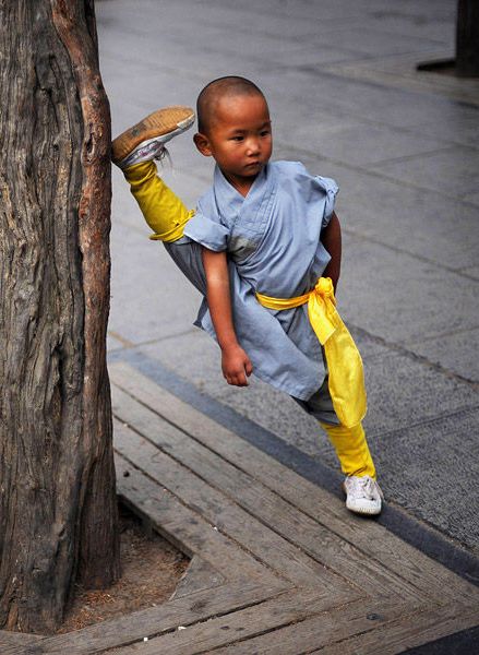 a little boy standing next to a tree