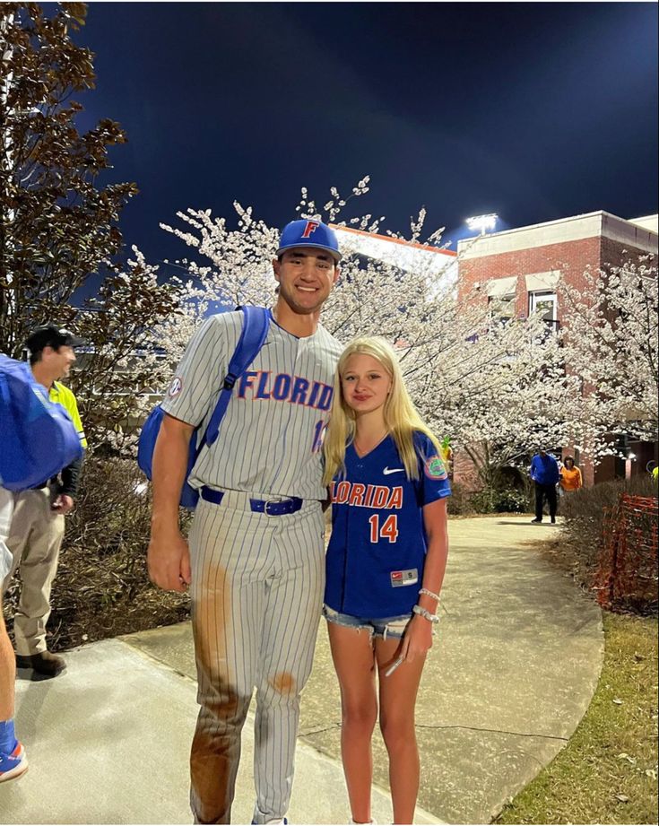 a man and woman in baseball uniforms posing for a photo on the sidewalk at night