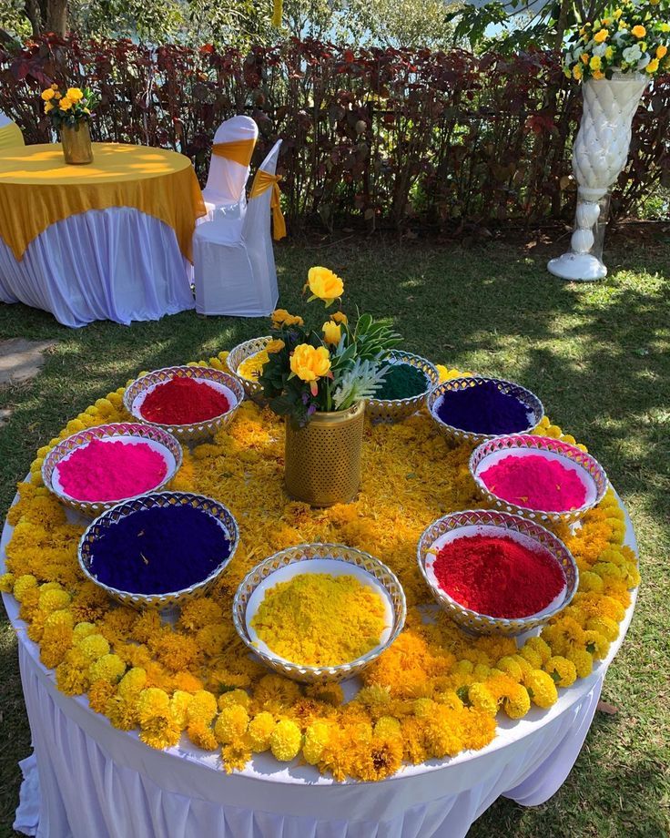 the table is covered with many different colored flowers and bowls filled with colorful powders