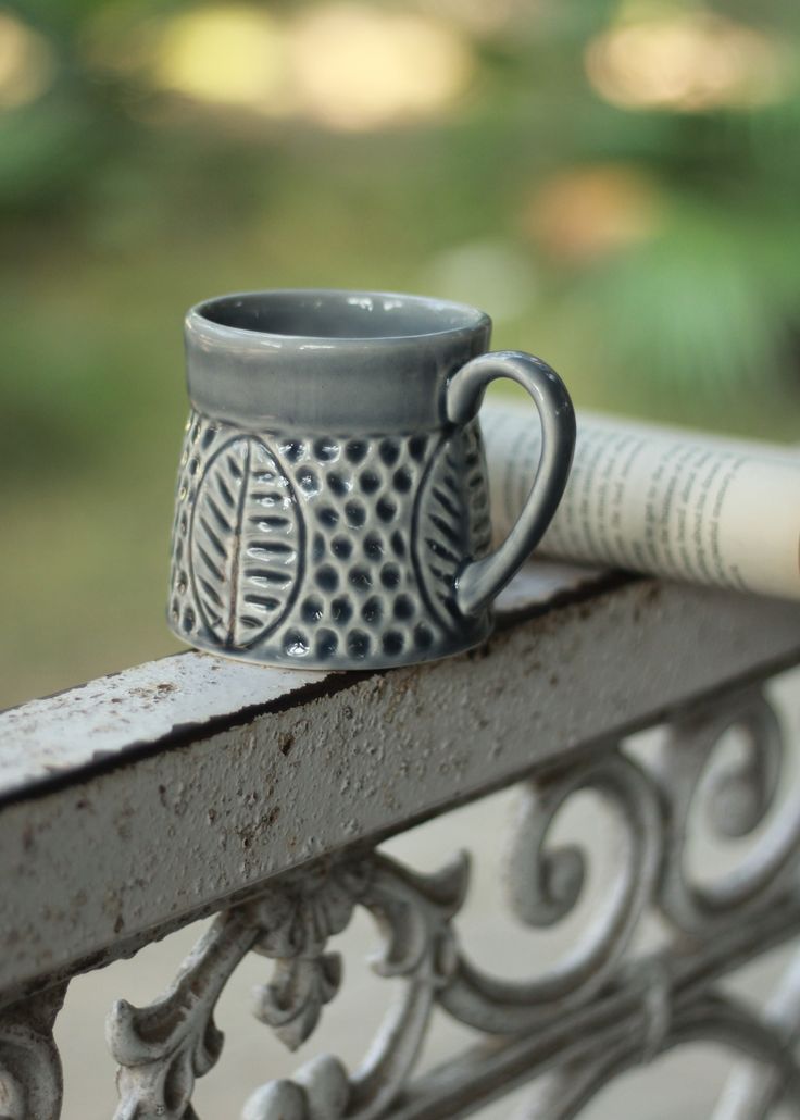 a coffee cup sitting on top of a metal bench next to a rolled up newspaper