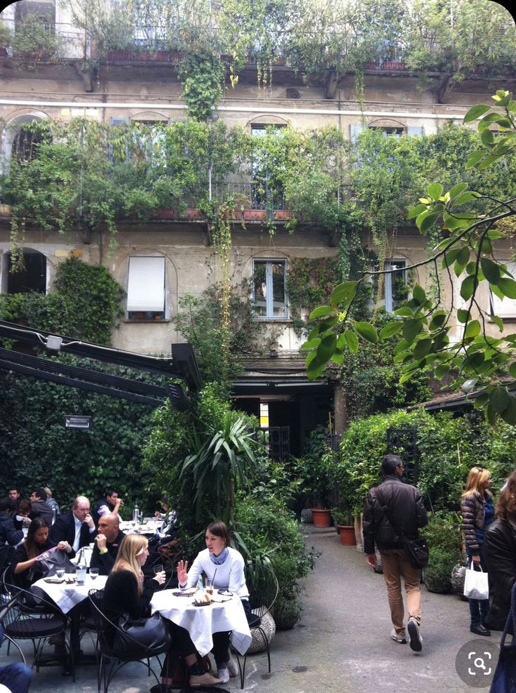 people are sitting at tables in an outdoor courtyard cafe with plants growing on the walls