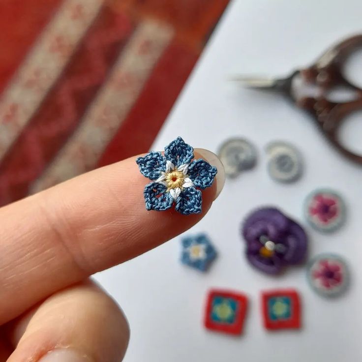 a hand holding a tiny blue flower on it's finger next to some buttons