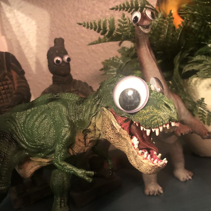 toy dinosaurs with fake eyes and plants in the background